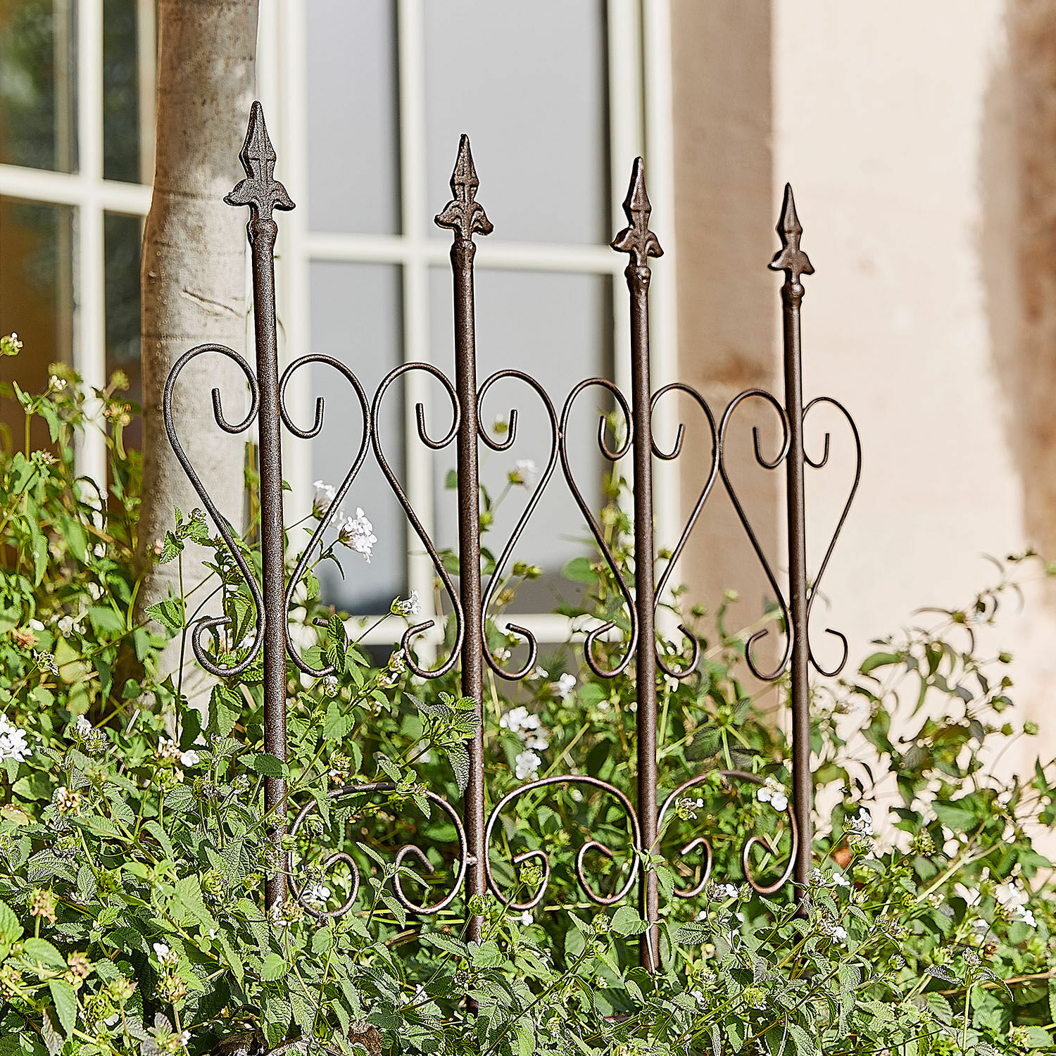 Trellis Nectarise Decoratief metalen tuinhek in roestbruin met hartmotief, omgeven door groene planten en witte bloemen
