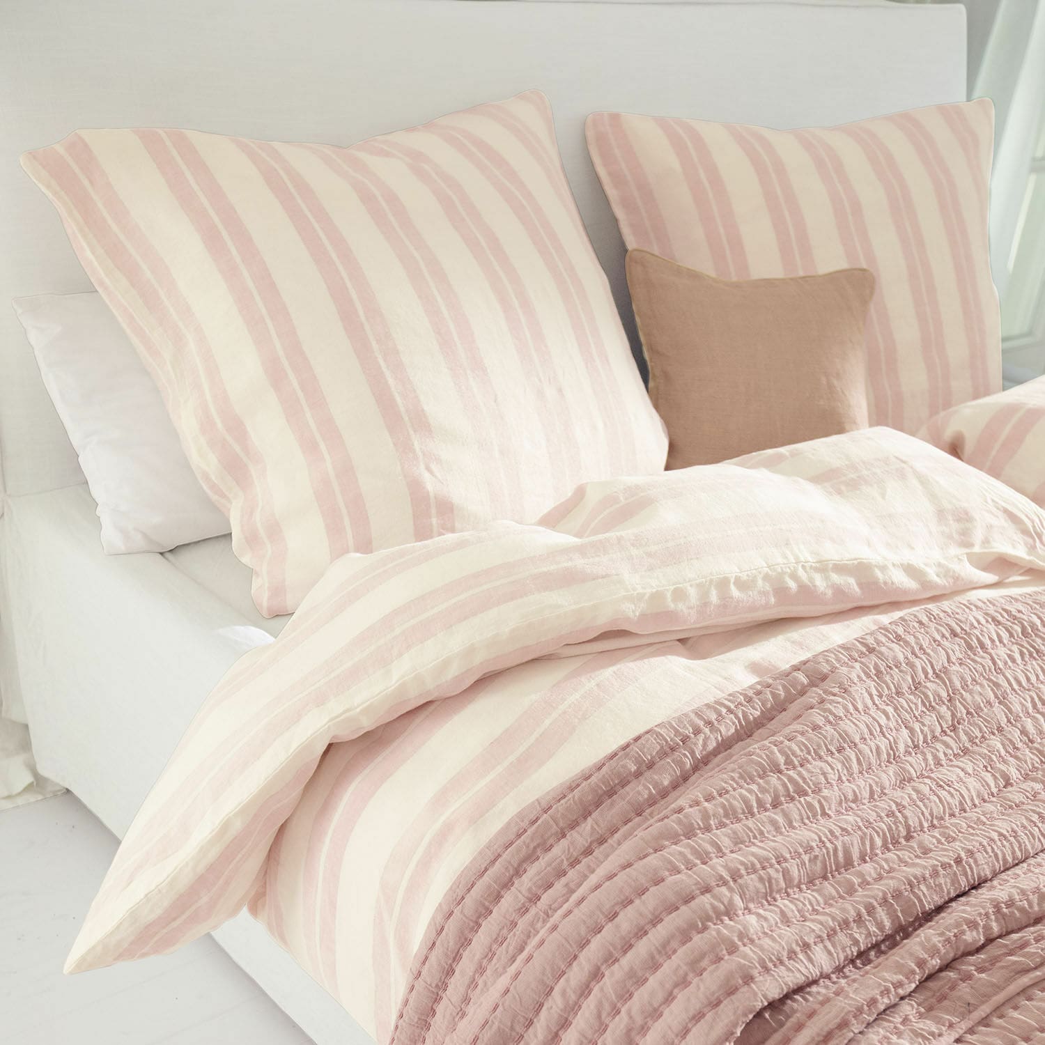 Parure de lit Dordogne Parure de lit en coton rayée rose et crème avec couverture rose douce sur un lit dans une chambre claire