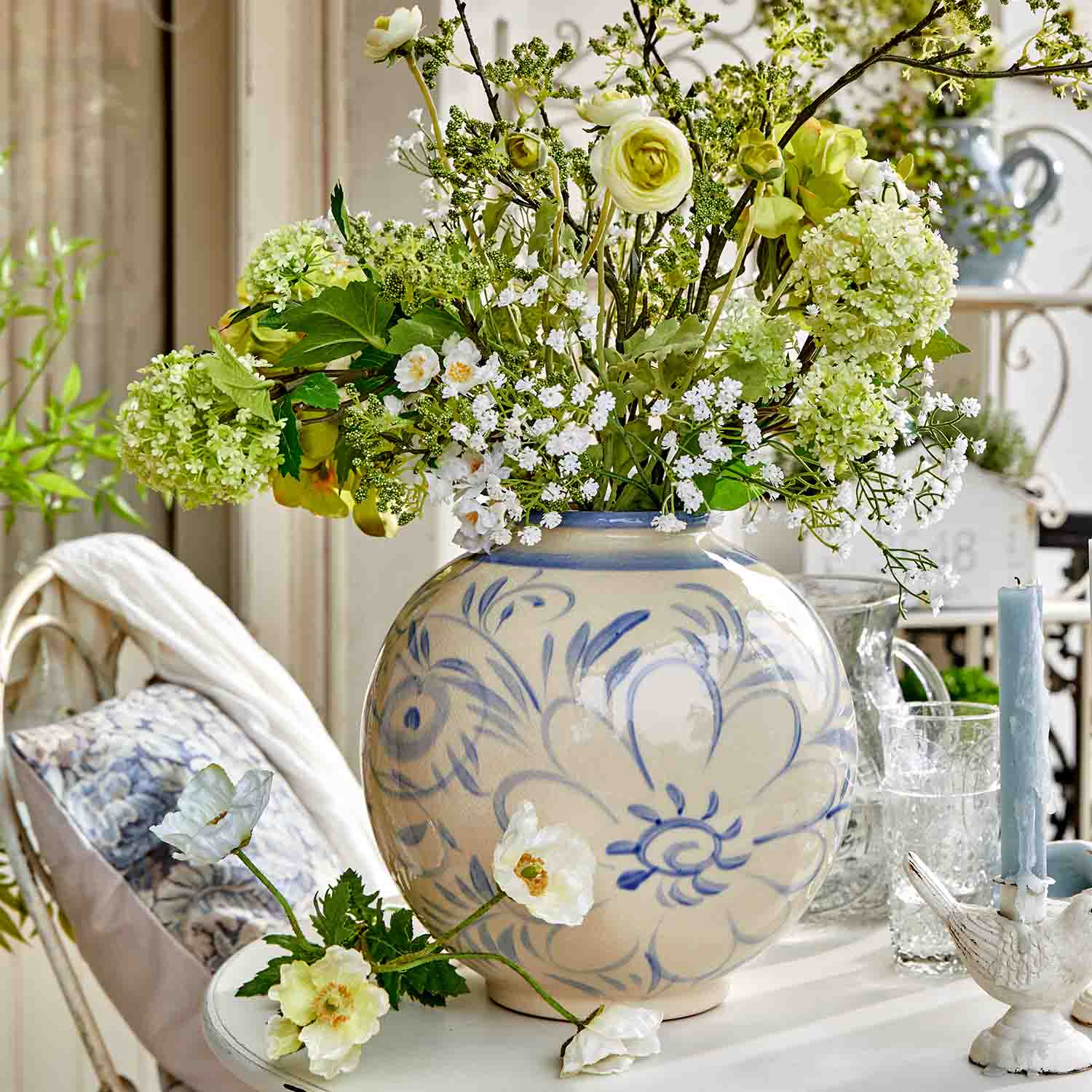 Vase en céramique ronde avec motif floral bleu et bouquet de fleurs vertes et blanches sur une table