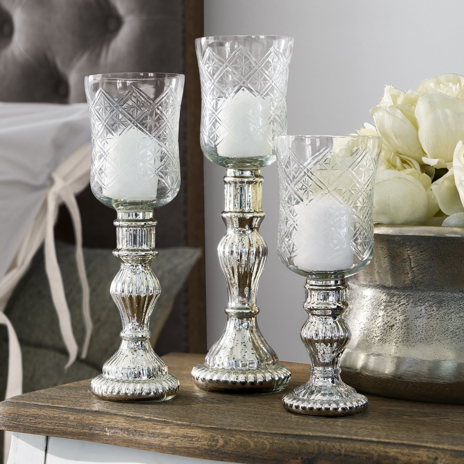 Set van drie glazen kandelaren met zilverkleurige metalen voet op houten tafel