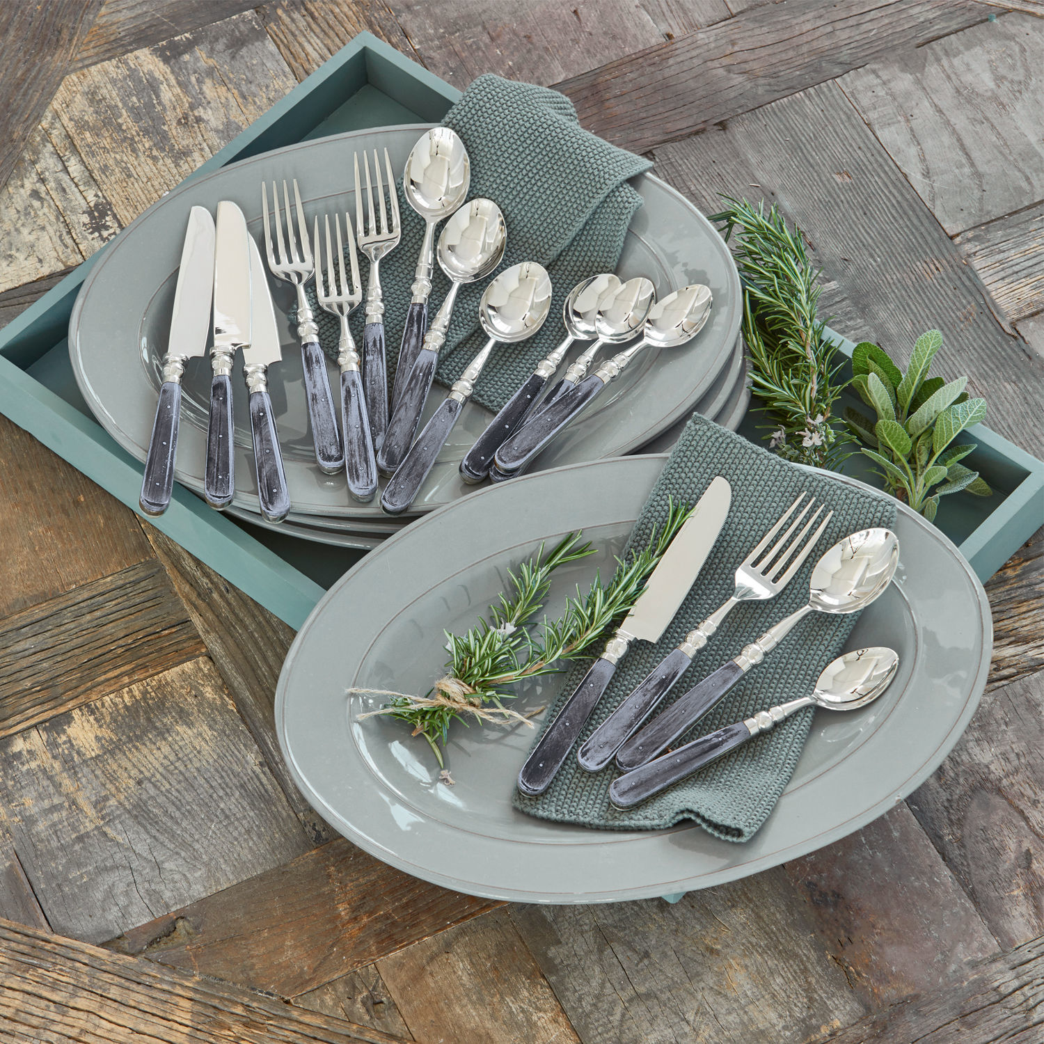 Couverts Bigeste Ensemble de couverts avec manches noirs et extrémités argentées sur assiettes grises avec serviettes vertes