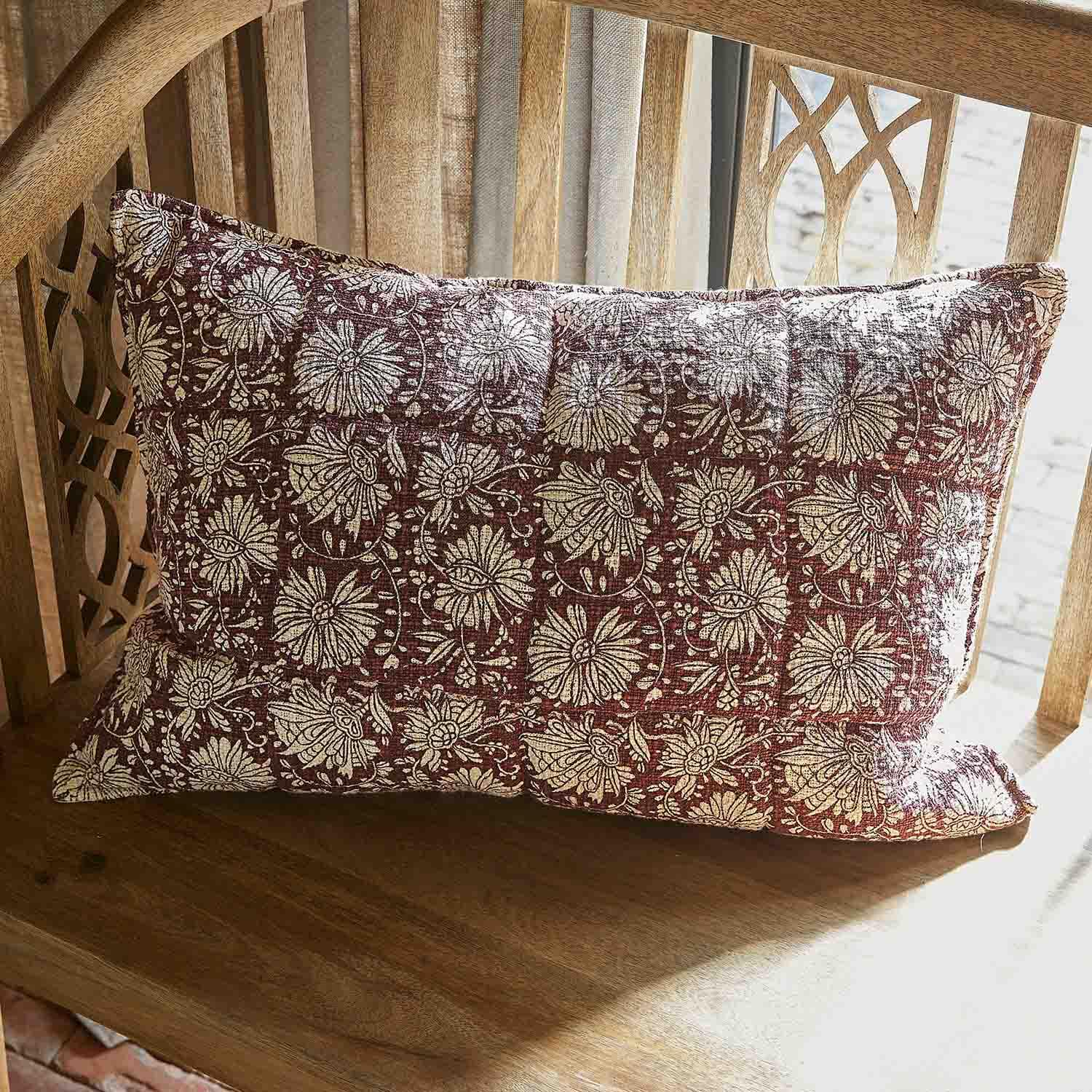 Decoratief katoenen kussen in bordeaux met crème bloemenpatroon op houten bank