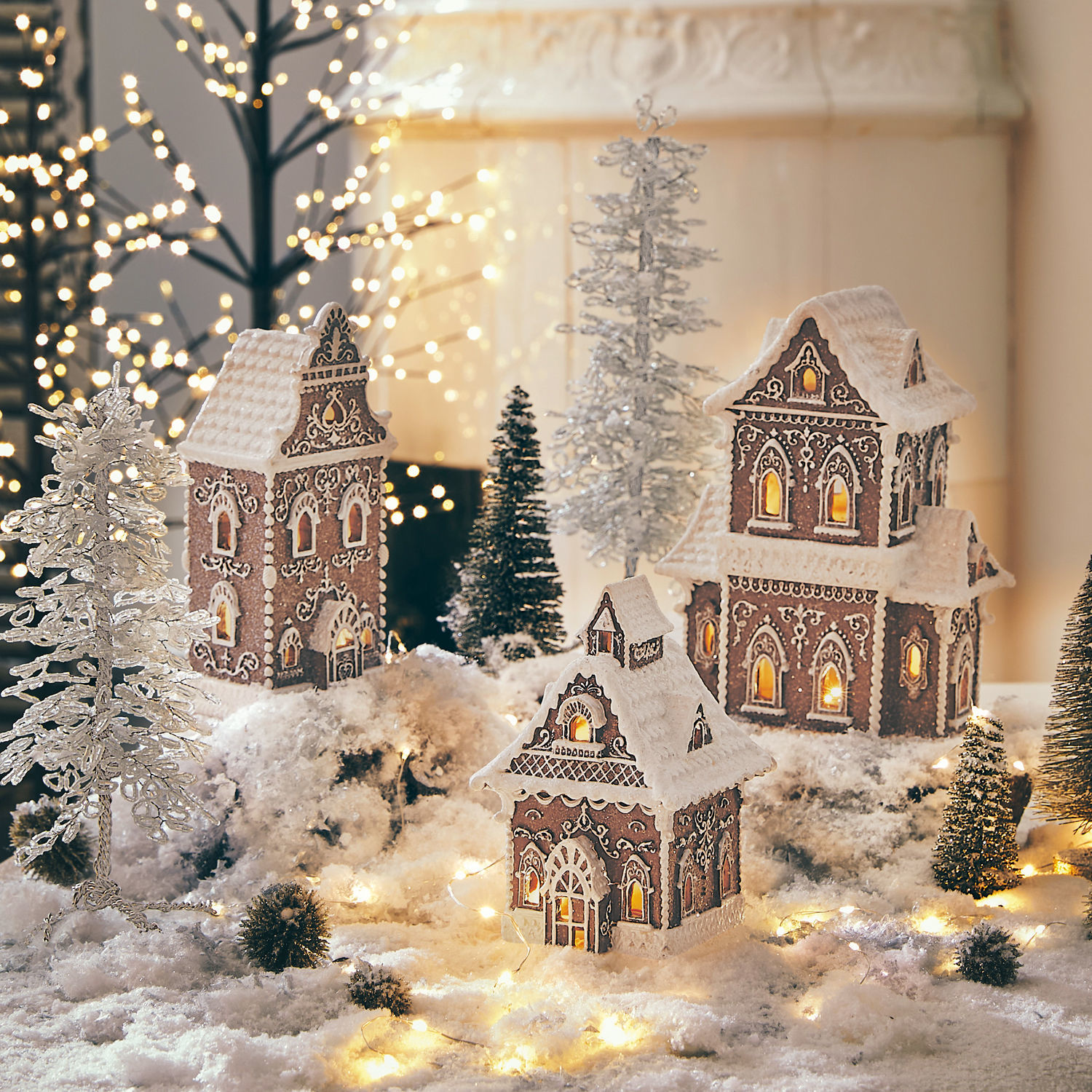 Lot de 3 maisons décoratives Anyama Maisons en pain d'épices décoratives avec glaçage blanc et lumières sur fond neigeux avec sapins