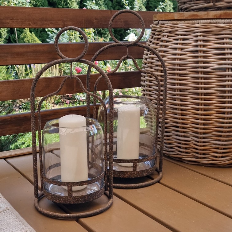 Deux lanternes décoratives en métal avec bougies blanches sur une table en bois dans un jardin
