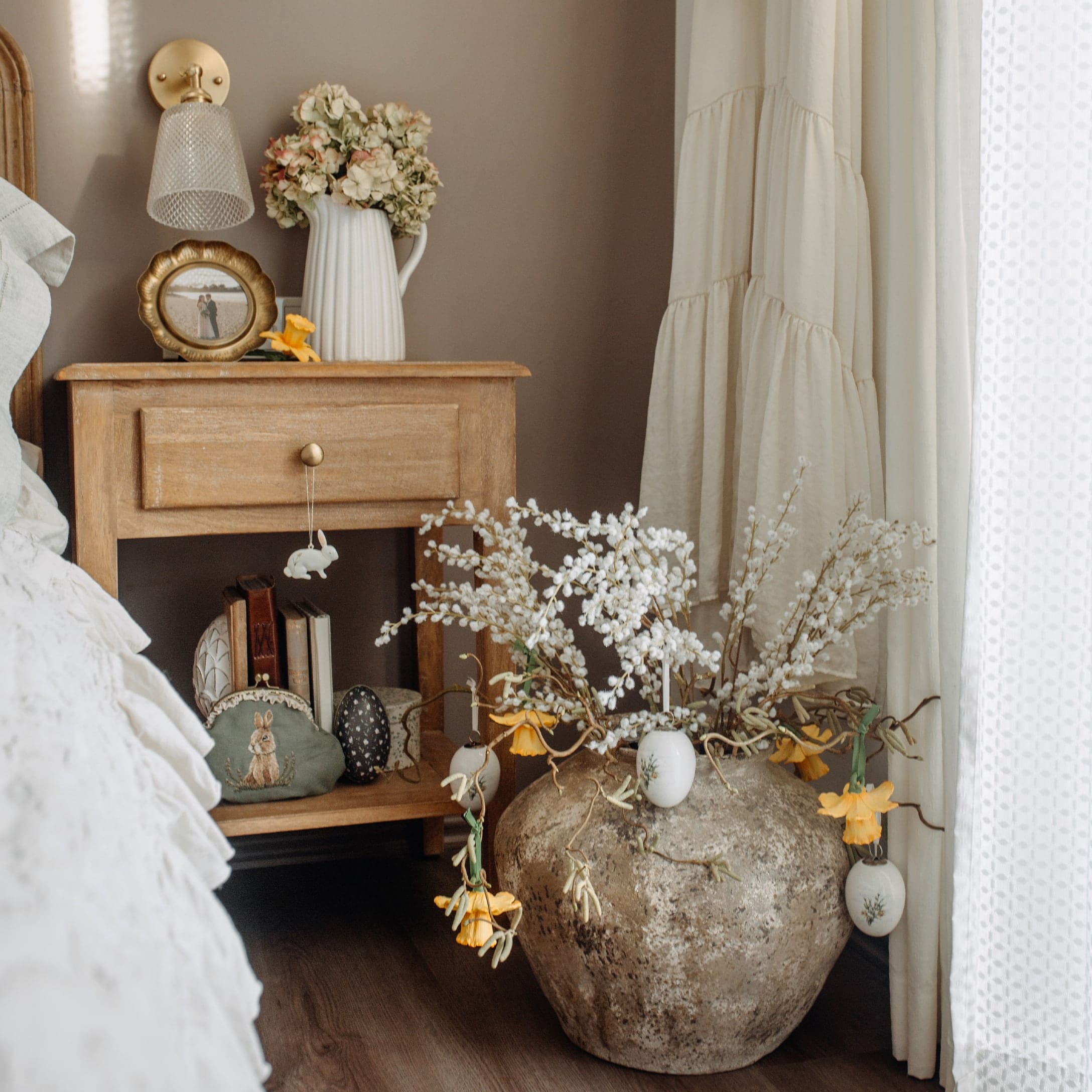 Rustieke houten nachtkastje met paasdecoraties en grote stenen vaas met bloemen