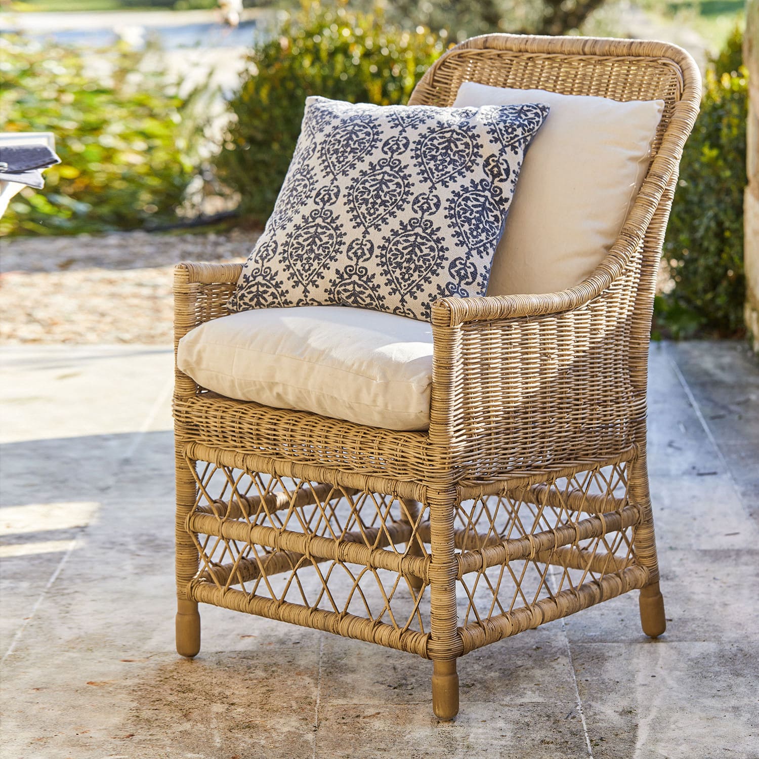 Fauteuil Giepmare Rotan stoel met crèmekleurige kussens en blauw patroon sierkussen, stijlvolle tuinmeubelen