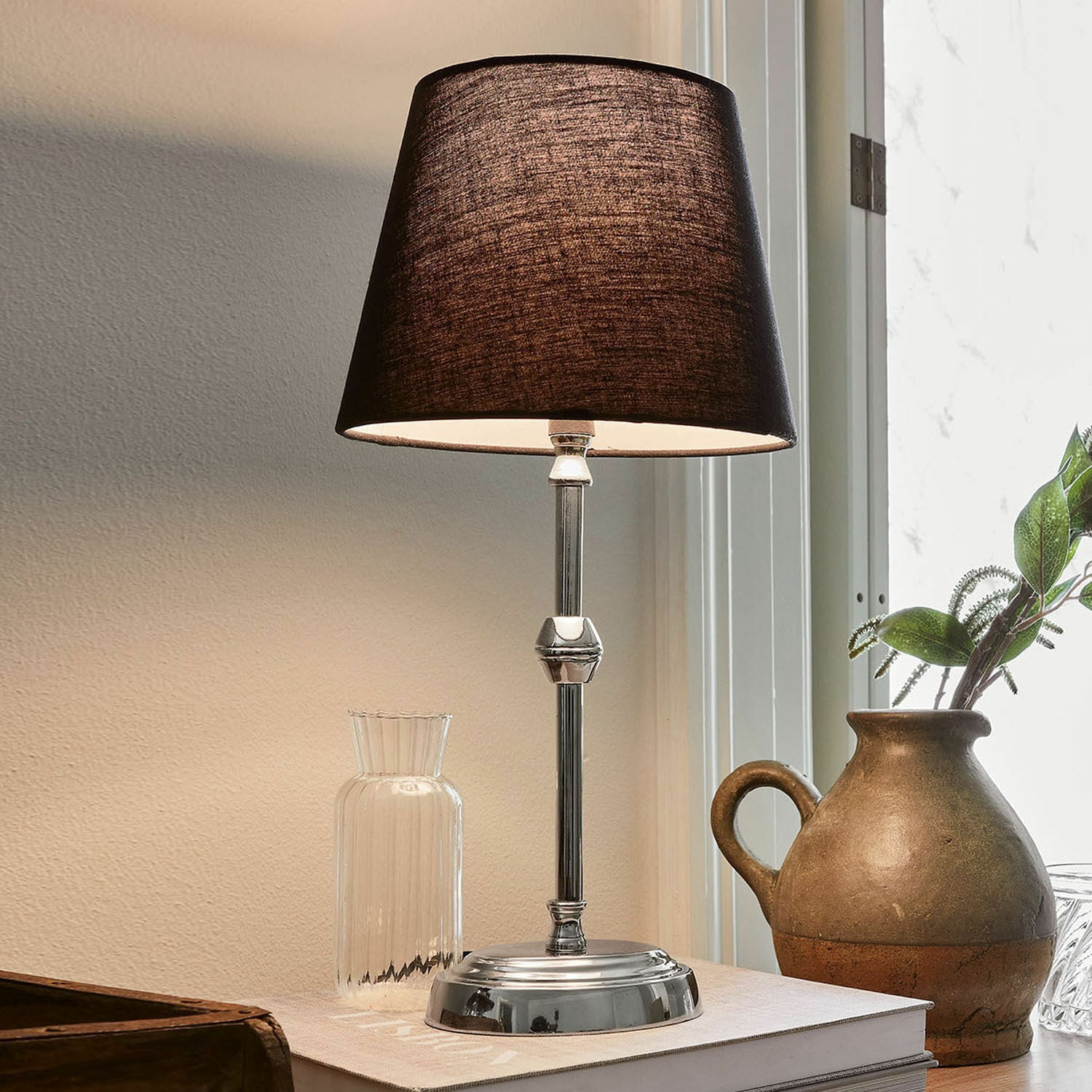 Elegante tafellamp met metalen voet en zwarte kap op bureau met decoratie