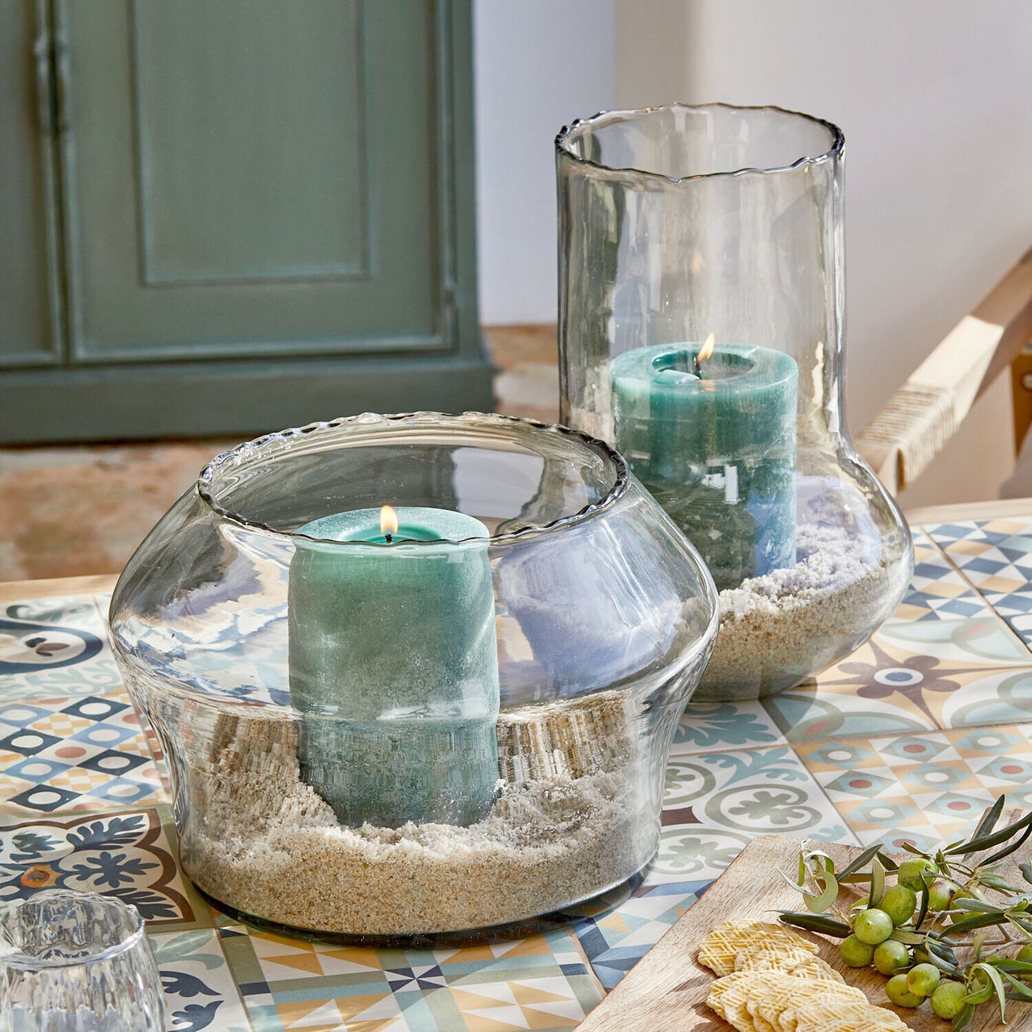 Bougeoirs en verre avec bougies vertes et sable sur une table colorée à motifs décoratifs