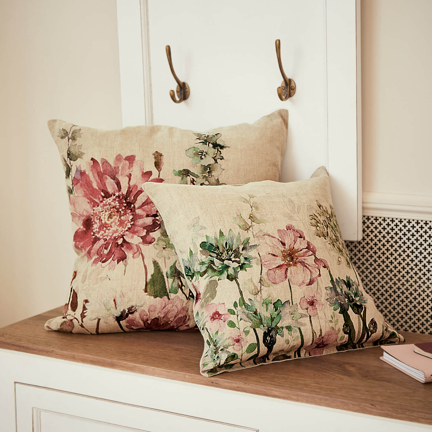 Twee linnen sierkussens met pastelkleurige bloemenprint op een houten oppervlak voor interieurdecoratie