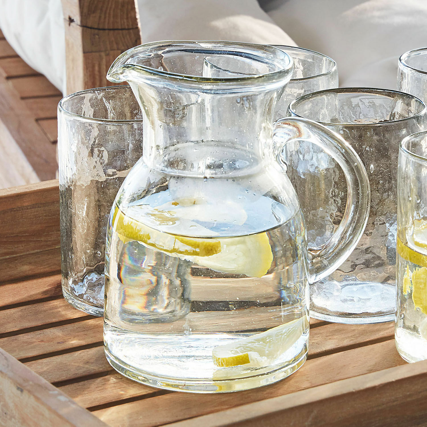 Carafe en verre avec poignée et tranches de citron sur plateau en bois pour servir des boissons