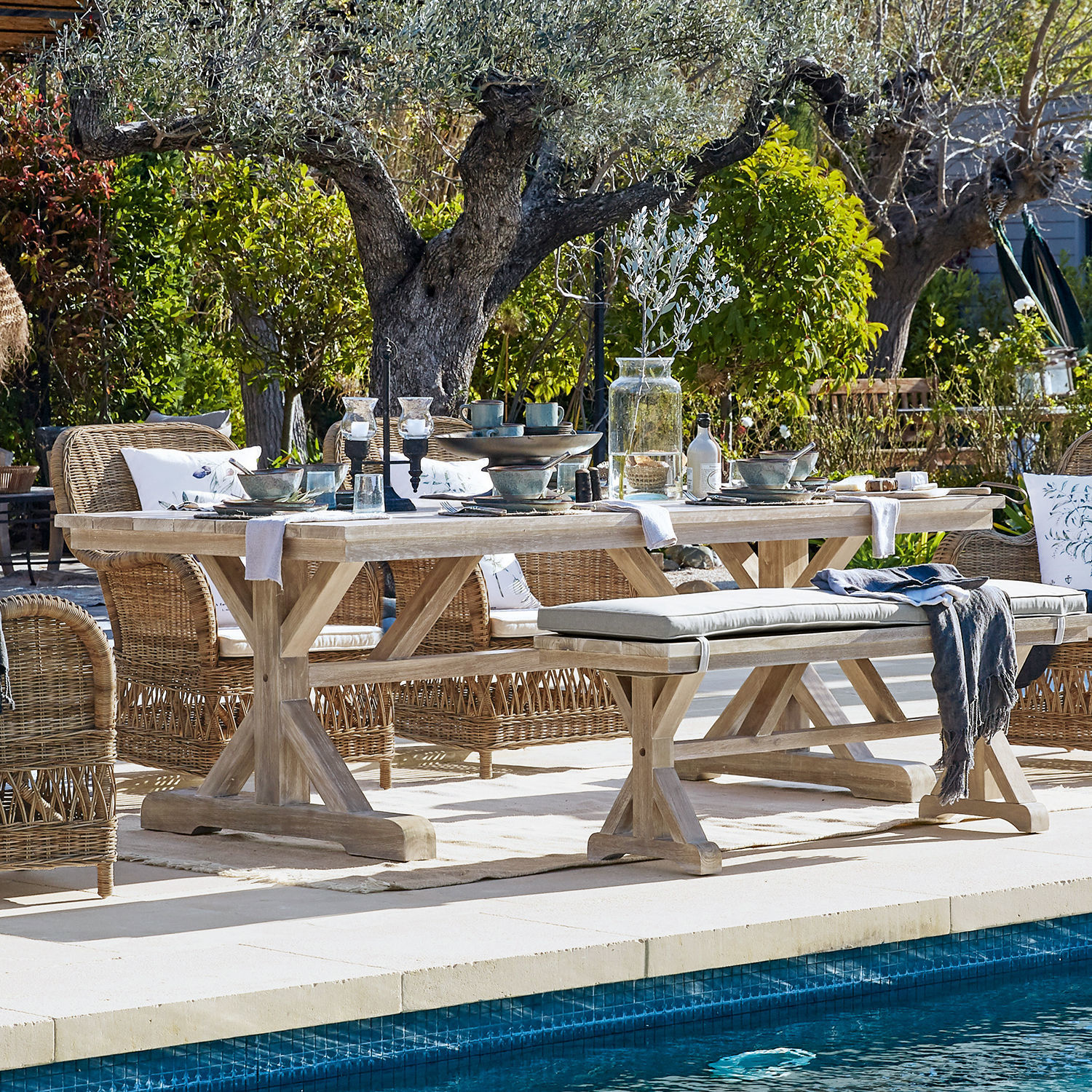Table FSC®-100% Graslin Table de jardin en bois clair avec chaises en osier près de la piscine dans un cadre naturel verdoyant