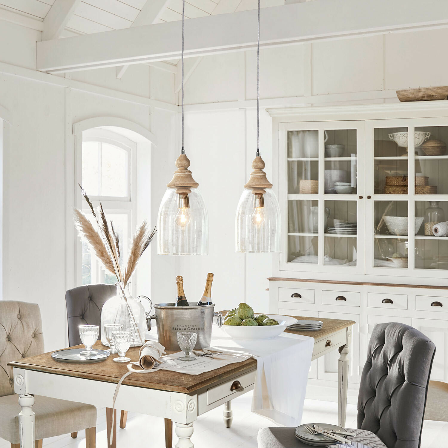 Rustieke eetkamer met witte houten tafel, grijze gestoffeerde stoelen en vitrinekast met rieten decoratie
