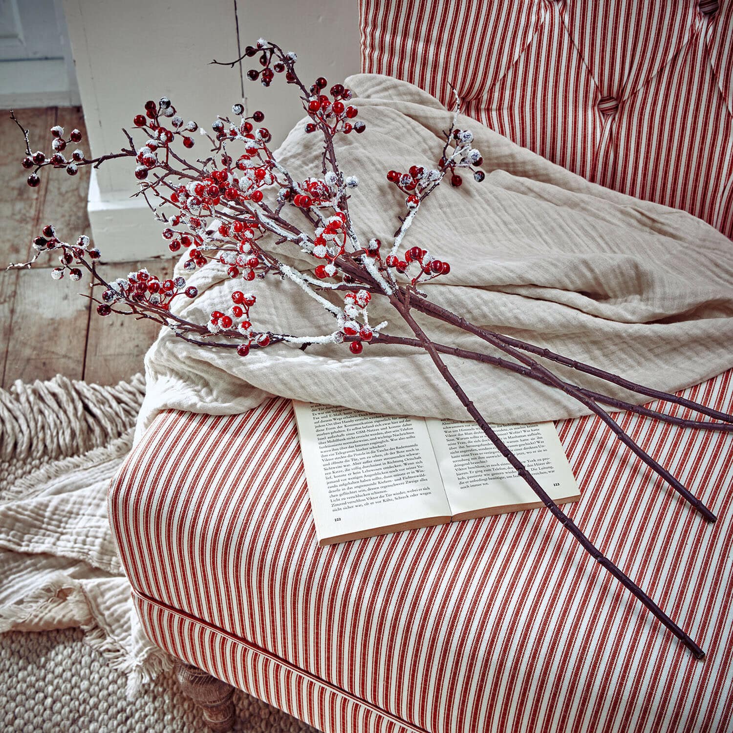 Decoratieve takken met rode bessen en sneeuw-effect op rood-wit gestreepte stoel met open boek