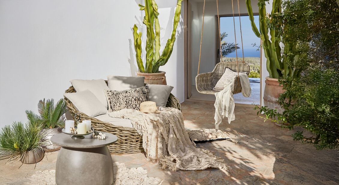 Ensemble de meubles en rotin beige avec coussins et plaid sur terrasse ensoleillée vue mer