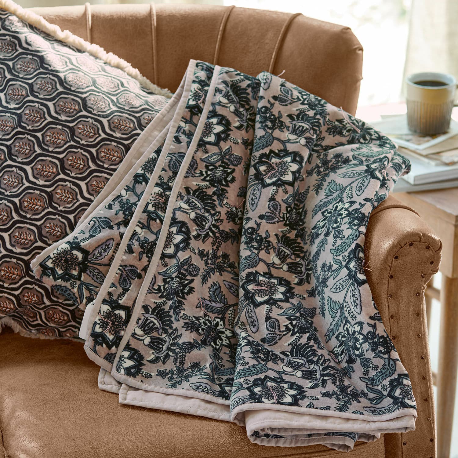 Plaid Elarion Plaid doux à motif floral gris posé sur un canapé beige avec coussin décoratif à motifs