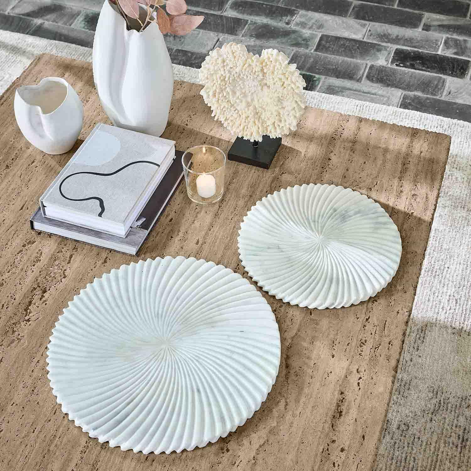 Deux assiettes décoratives blanches en marbre avec motif ondulé sur table beige avec livres et bougie