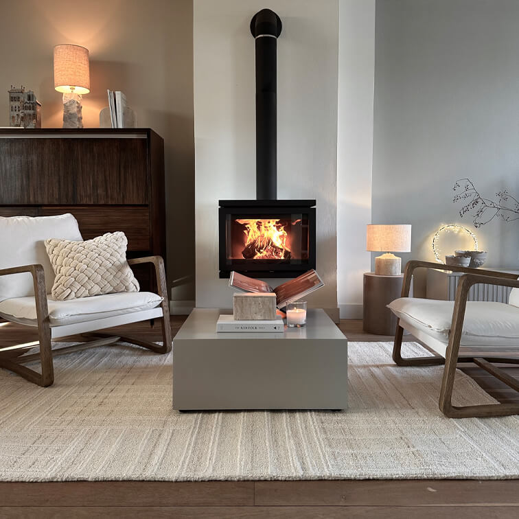 Salon moderne avec cheminée à bois, tapis beige et deux fauteuils en bois avec coussins blancs