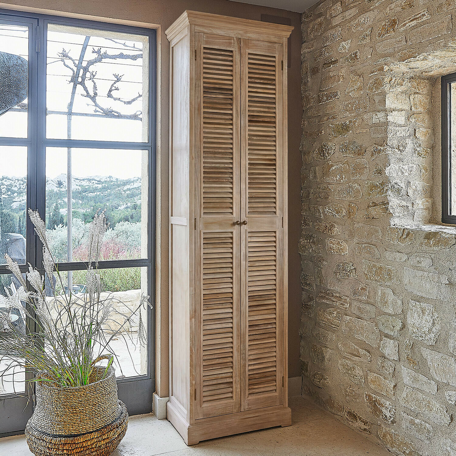 Hoge kast van natuurlijk hout met lamellen deuren in rustieke ruimte met stenen muur