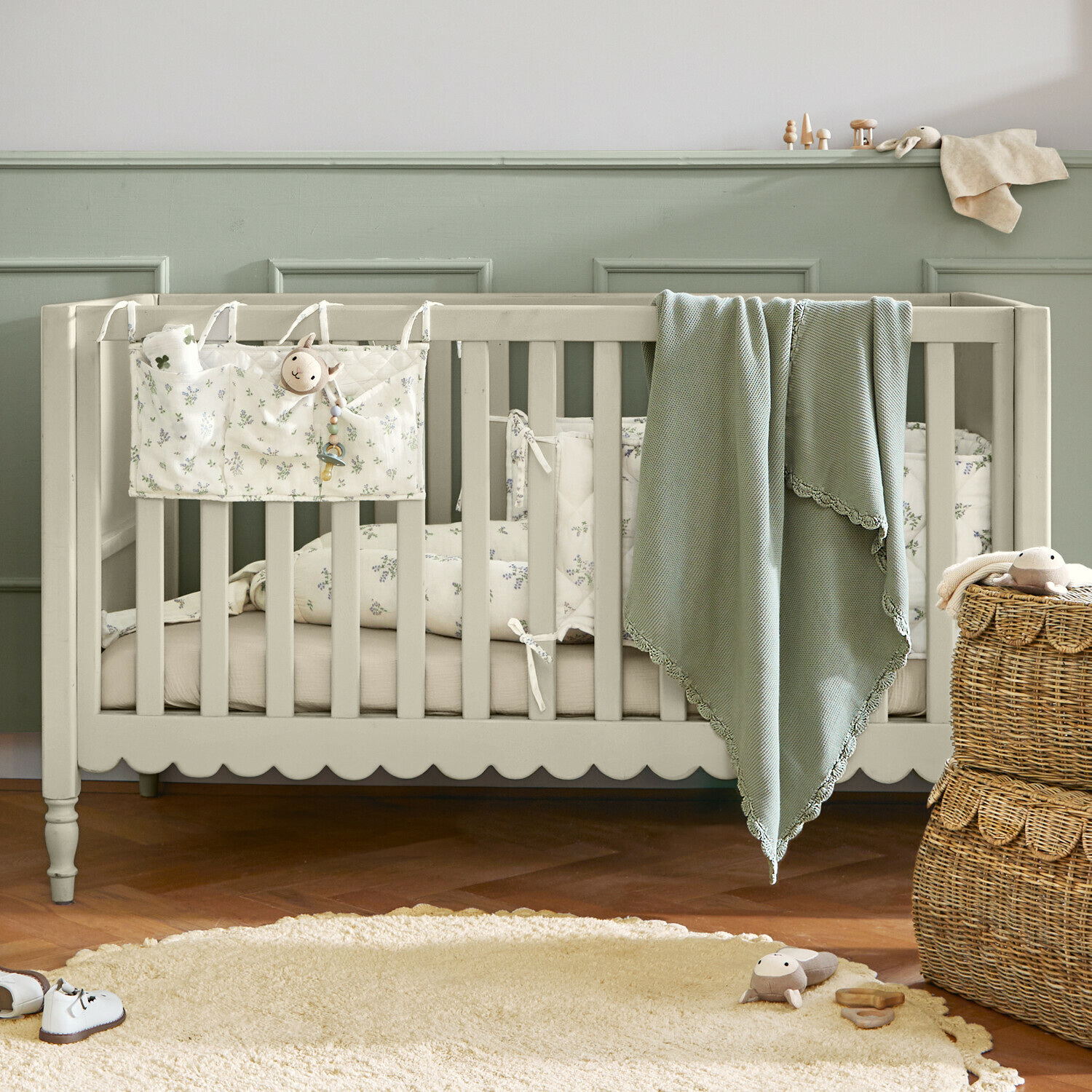 Lit bébé Leily Lit bébé en bois beige avec couverture verte et literie à motif floral dans une chambre d'enfant chaleureuse