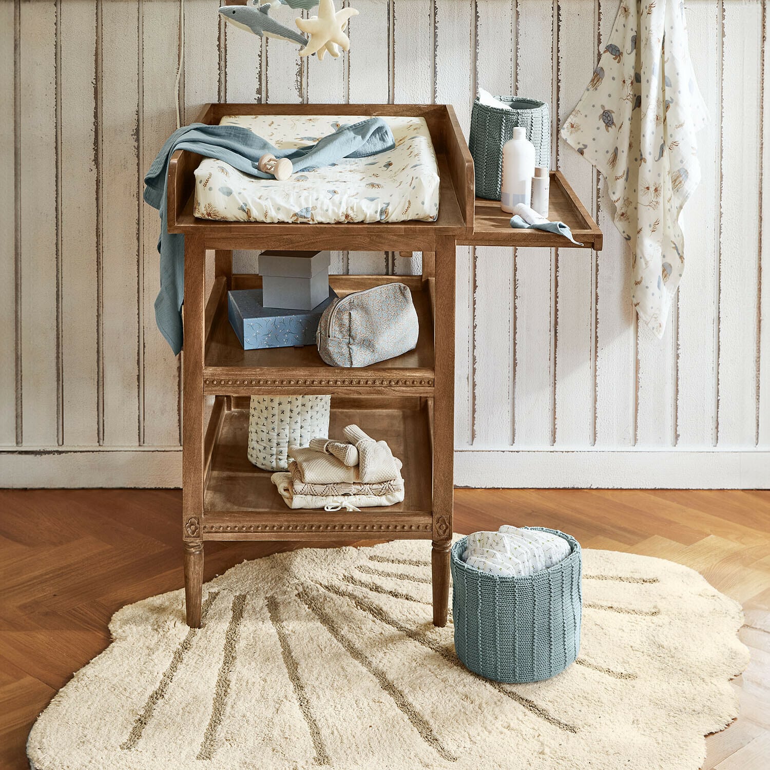 Vloerkleed Vellaro Houten commode met zacht matras en blauwe luiermand in kinderkamer