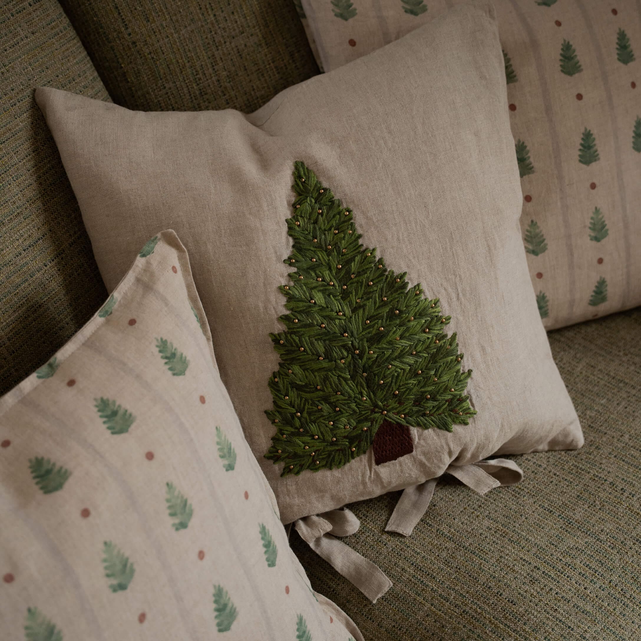 Coussin en lin beige avec arbre vert brodé et perles décoratives sur canapé texturé