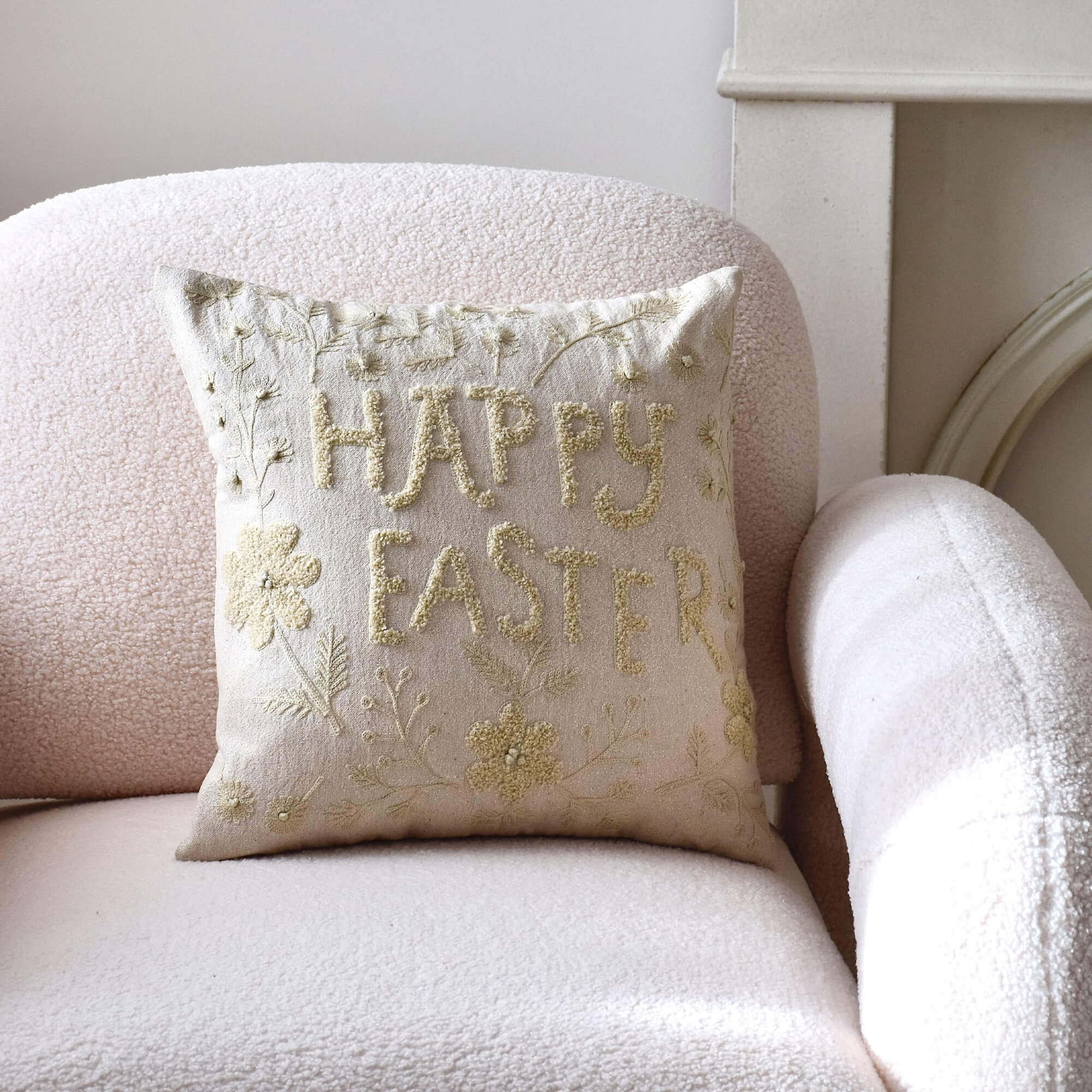 Coussin décoratif beige avec broderie Happy Easter sur fauteuil clair, motif pastel de Pâques