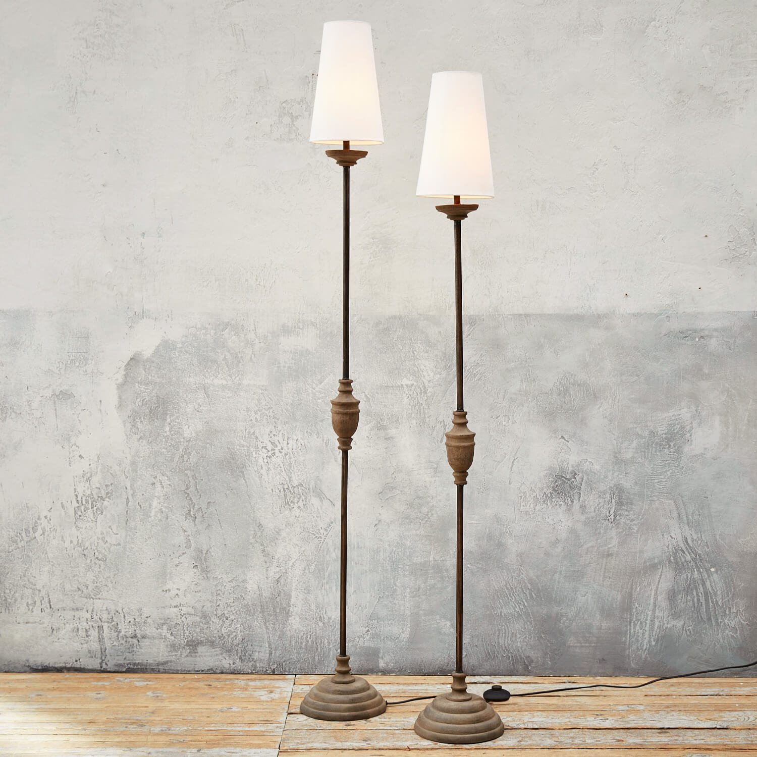 Twee hoge vloerlampen met metalen voet en witte lampenkappen op een lichte houten vloer