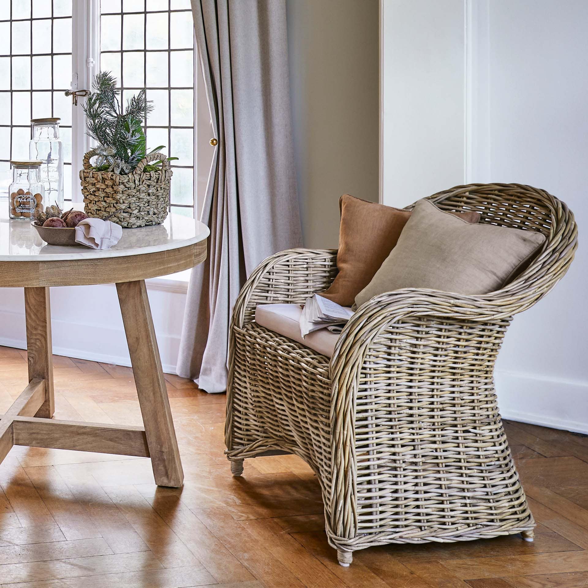Fauteuil en rotin naturel avec coussins beige dans un salon lumineux au sol en bois