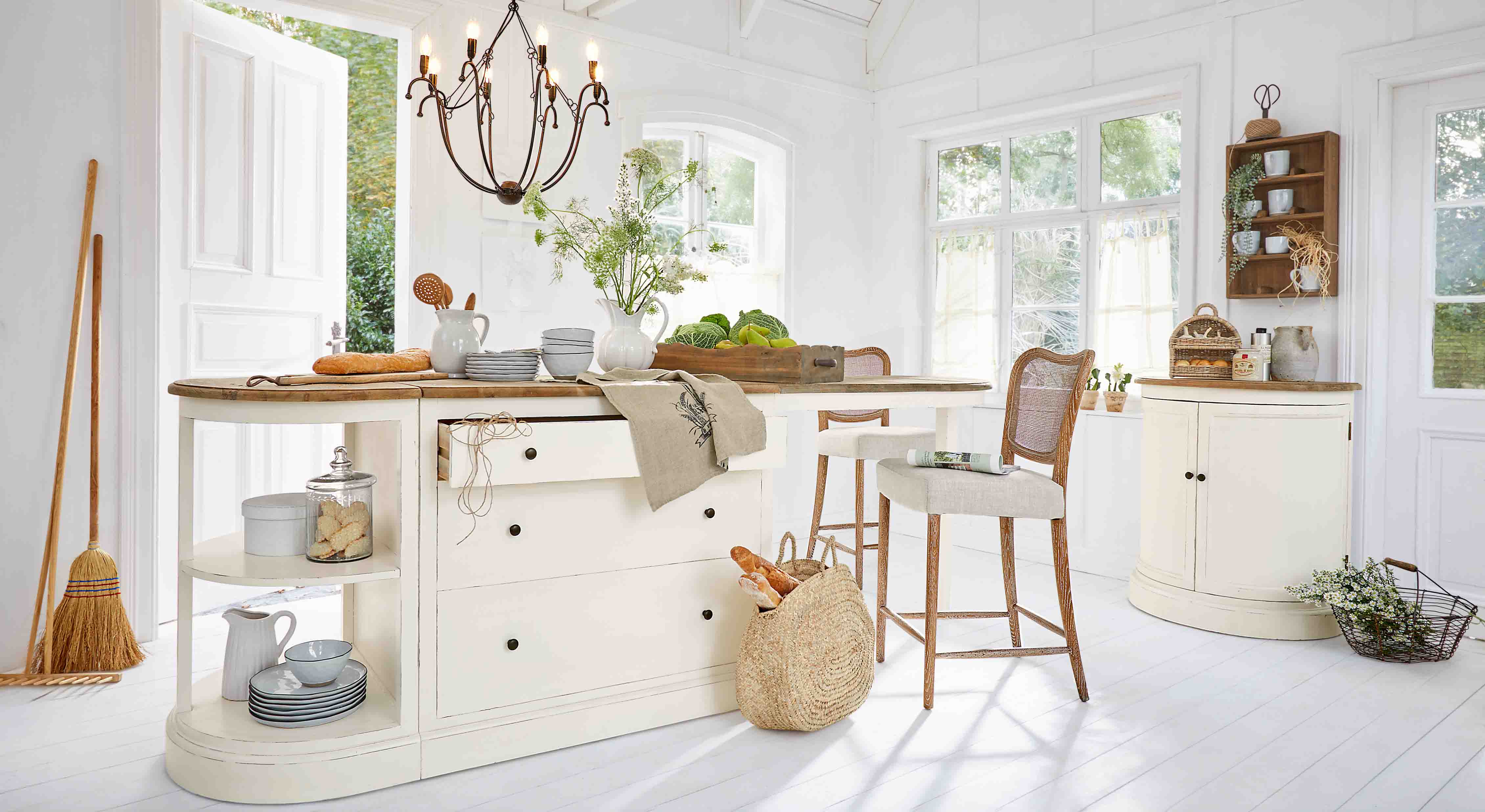 Cuisine lumineuse avec îlot blanc à plateau en bois et chaises en osier, décorations naturelles