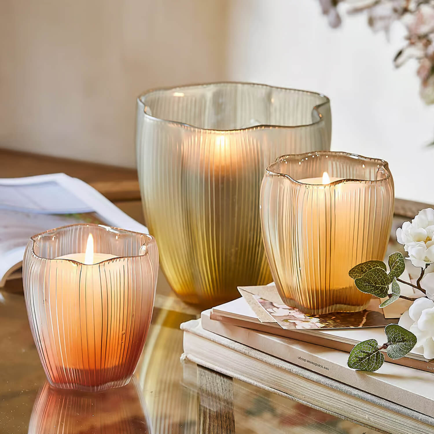 Ensemble de trois photophores en verre aux tons chauds ambrés sur une table avec livres et fleurs