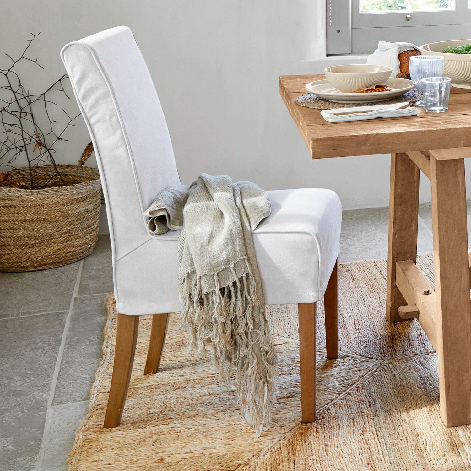 Chaise rembourrée blanche avec pieds en bois et plaid beige sur tapis naturel en jute