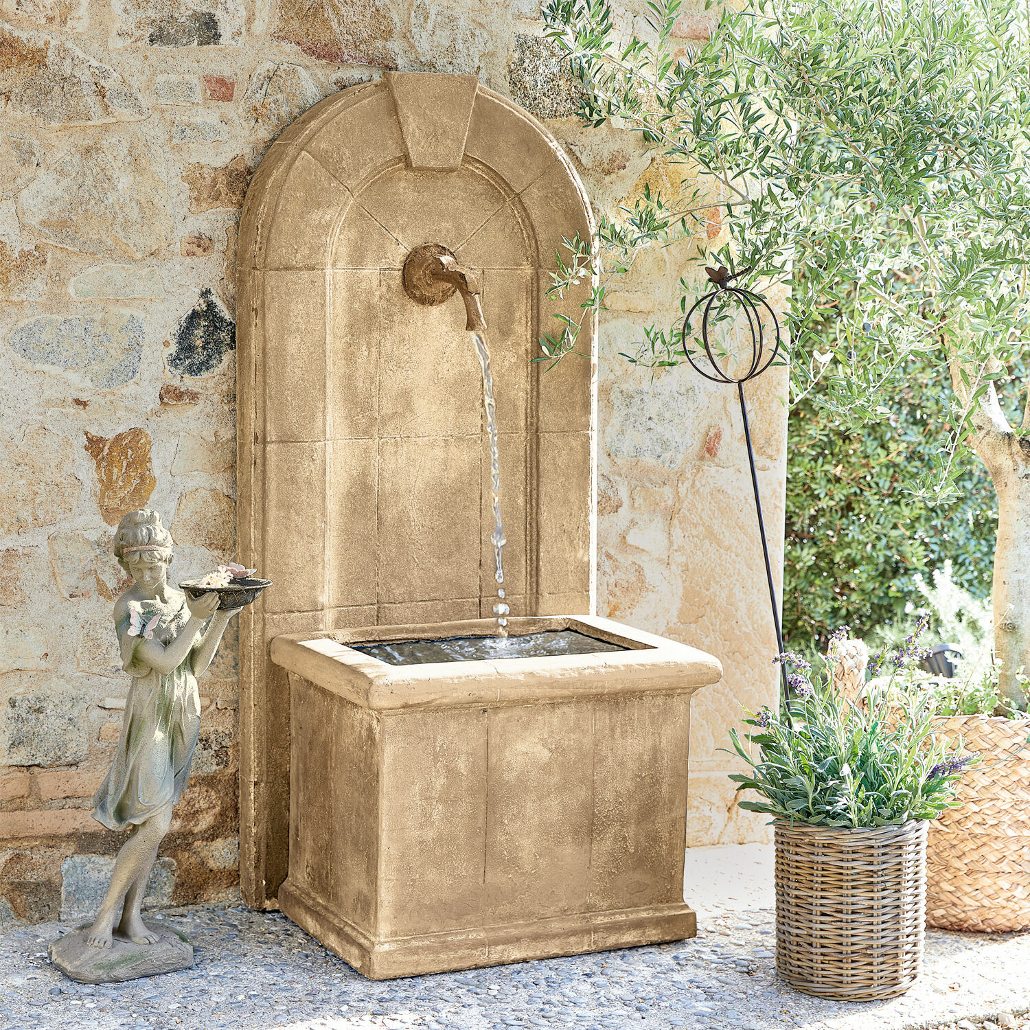 Fontaine Ginette Fontaine de jardin décorative en pierre beige avec eau et statue de fillette devant un mur en pierre