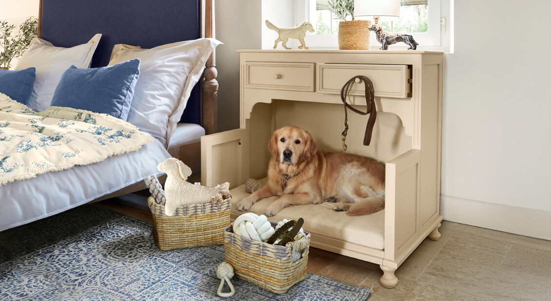 Beige houten kast met hondenmand en kussen naast bed met blauwe kussens in slaapkamer