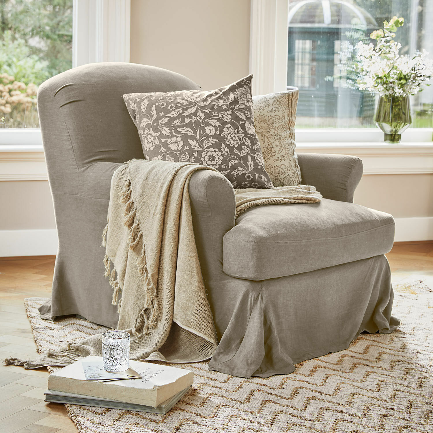 Fauteuil Vionnique Fauteuil beige en tissu avec coussins décoratifs et plaid sur tapis clair dans un salon lumineux