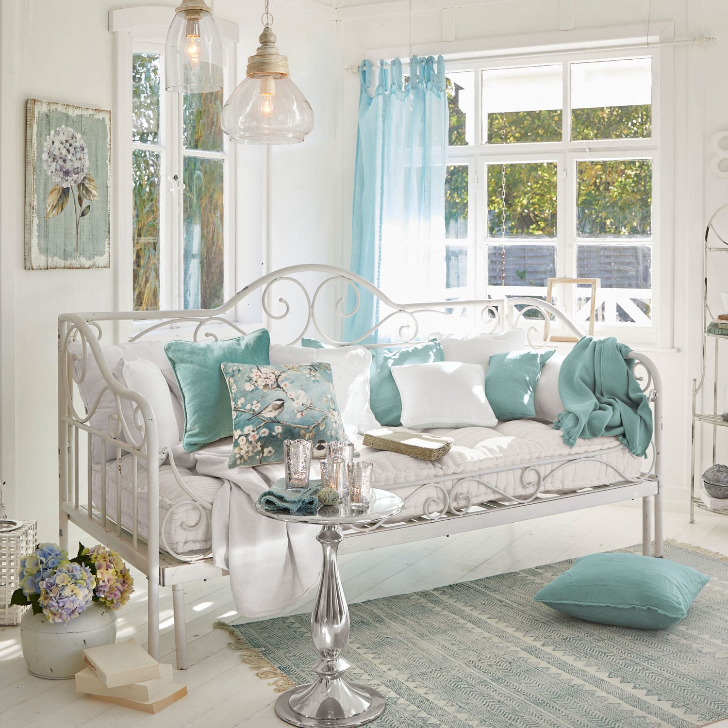 Bedbank Maditha Witte metalen bank met zachte kussens en turquoise accenten in lichte woonkamer met groot raam