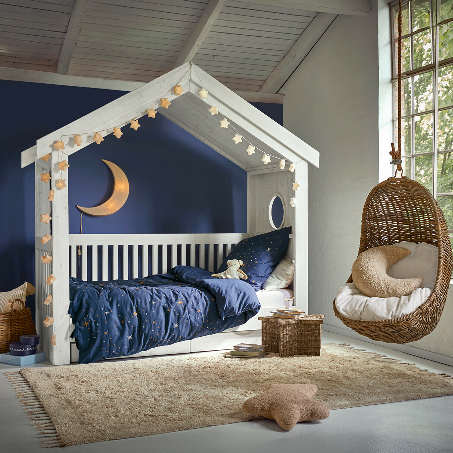 Vloerkleed Avenagh Wit houten kinderbed in huisvorm met donkerblauw sterrenbeddengoed en hangende rotan stoel in kinderkamer