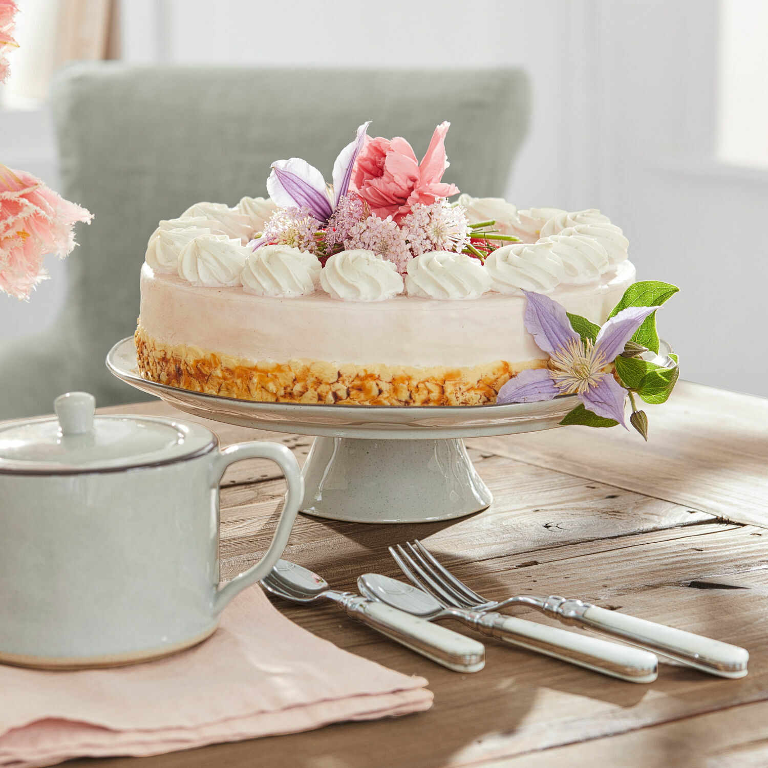 Plat Biarré Gâteau sur un plat en céramique avec crème et fleurs, couverts à manches blanches sur table en bois