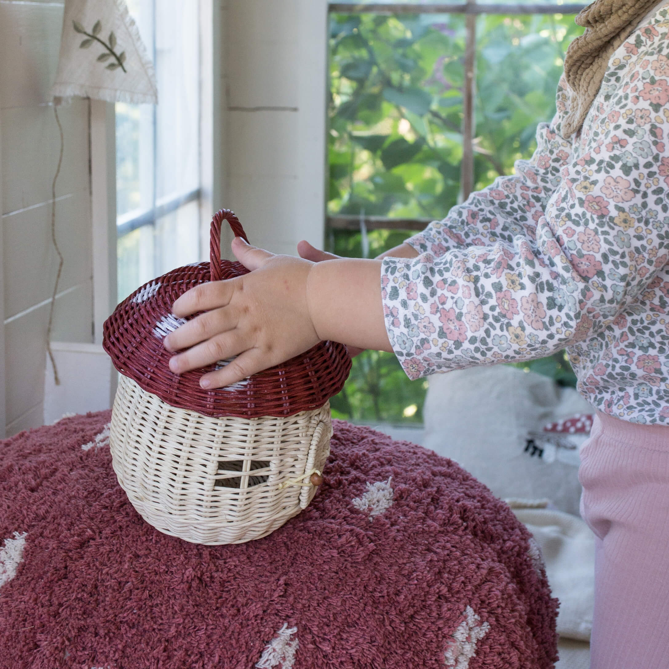 Enfant touchant un panier en osier en forme de champignon beige et rouge sur un tapis rose