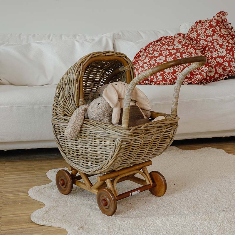 Poussette en osier avec roues en bois et peluches dans un salon clair avec canapé blanc