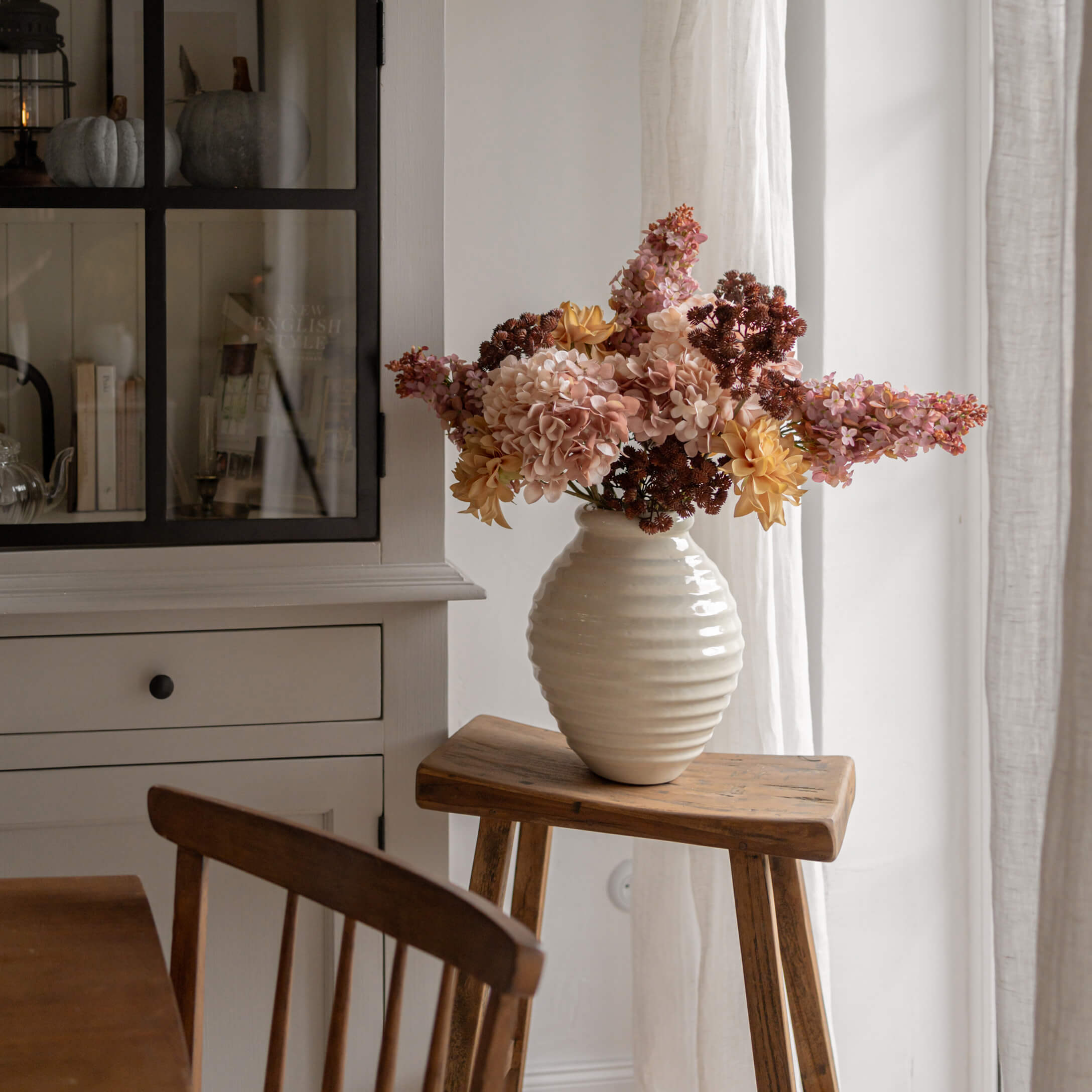 Witte albasten vaas met geel-roze bloemen op houten kruk in lichte kamer
