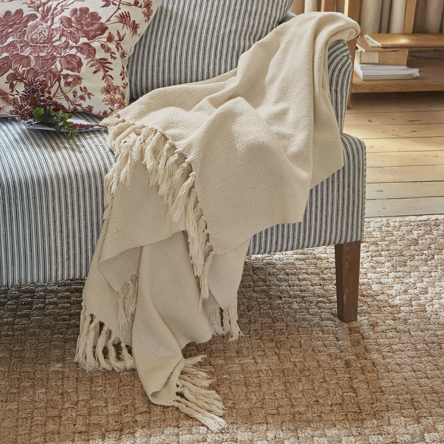 Plaid Skandira Plaid beige en tissu doux avec franges sur un canapé rayé gris dans un salon chaleureux