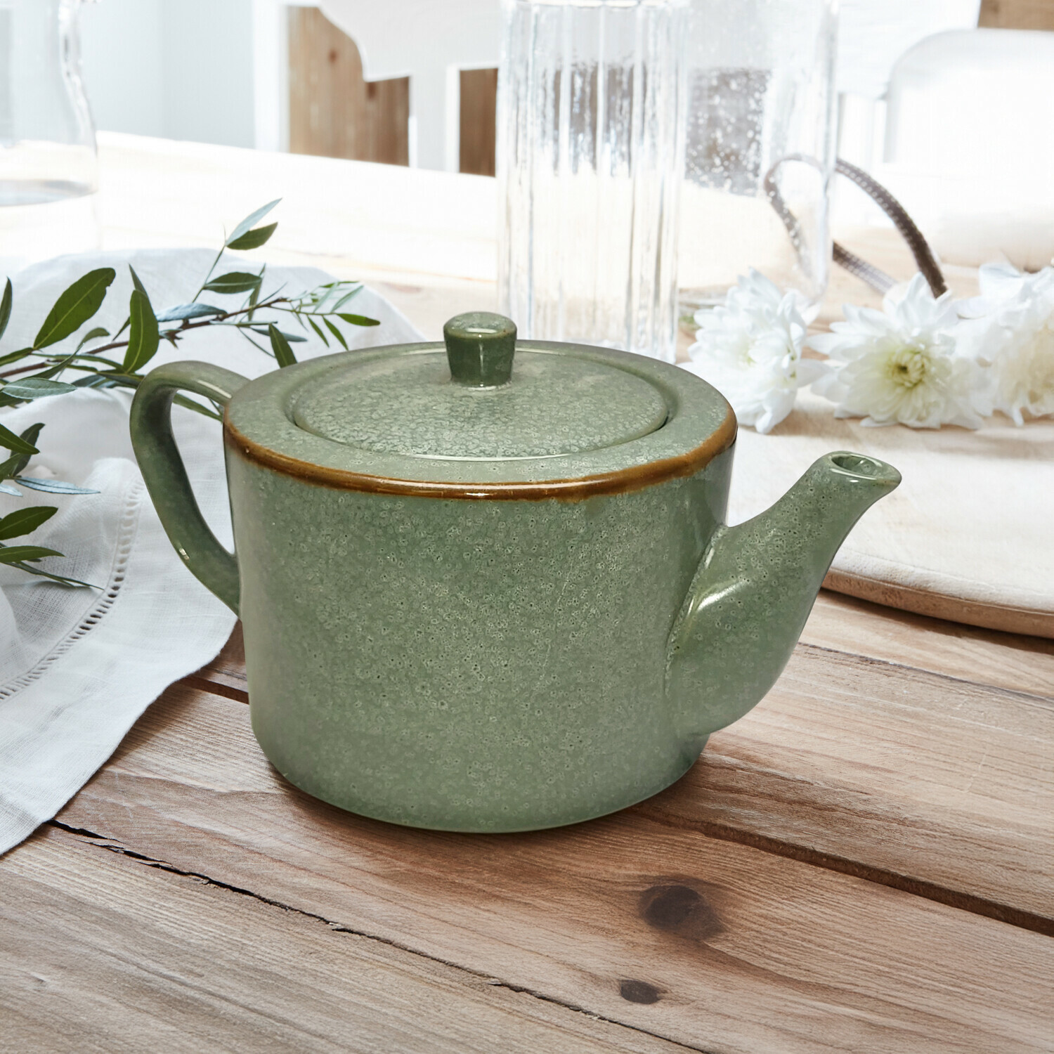 Théière Biarré Théière en céramique verte avec couvercle et bord brun posée sur une table en bois avec décoration florale