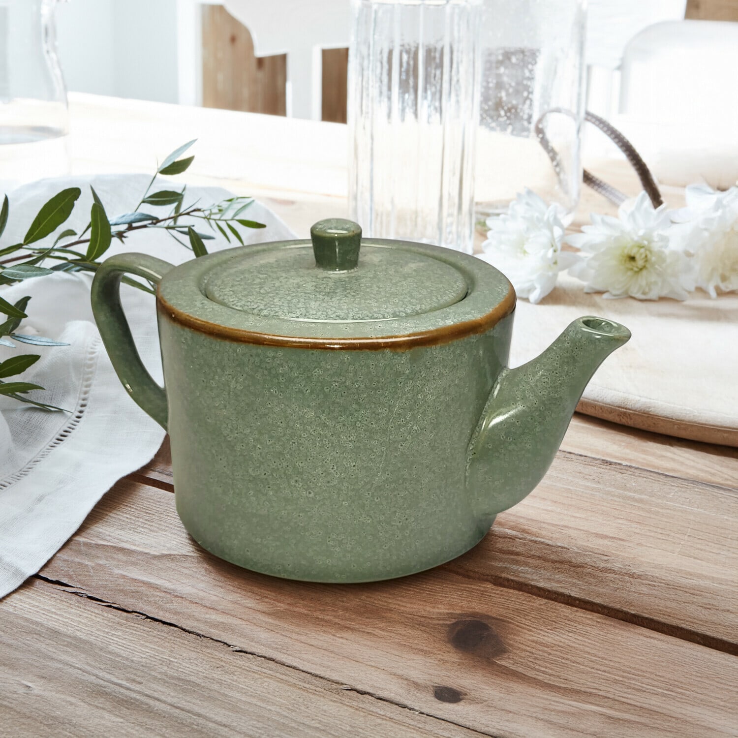 Théière Biarré Théière en céramique verte avec couvercle et bord brun posée sur une table en bois avec décoration florale