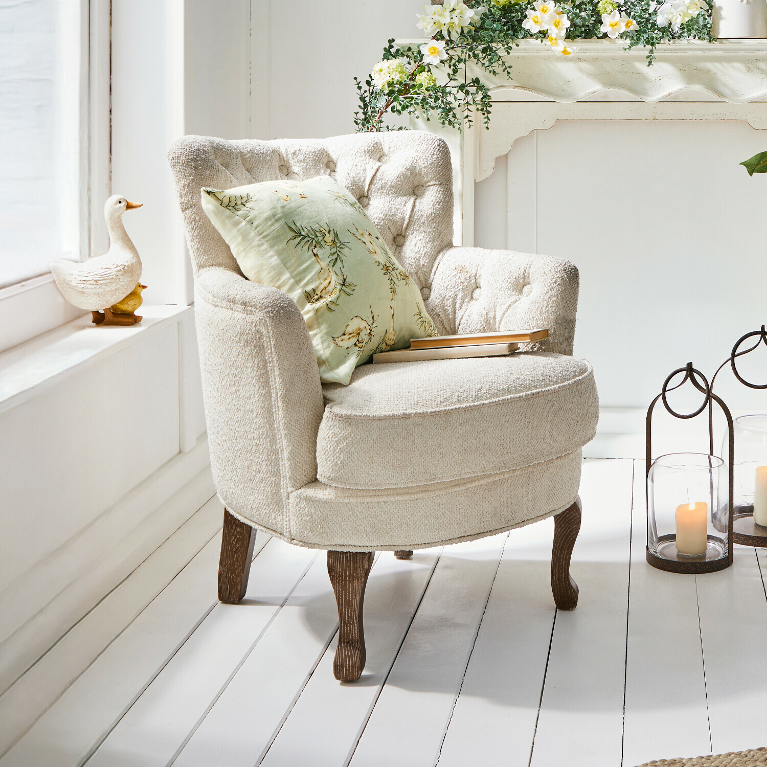 Fauteuil Calgary Fauteuil beige en tissu doux avec pieds en bois et coussin vert à motifs floraux dans un intérieur lumineux