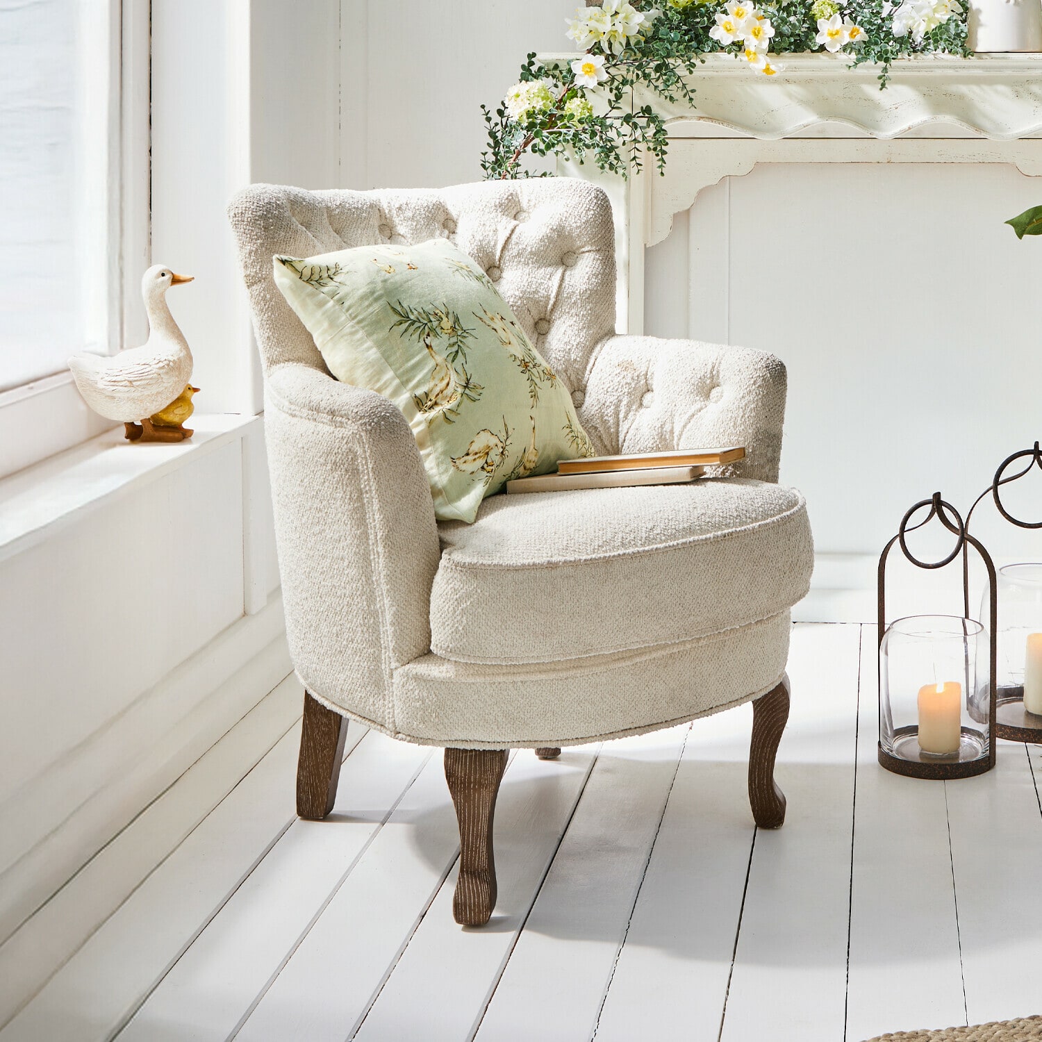 Fauteuil Calgary Beige fauteuil van zachte stof met houten poten en groen bloemenkussen in lichte kamer