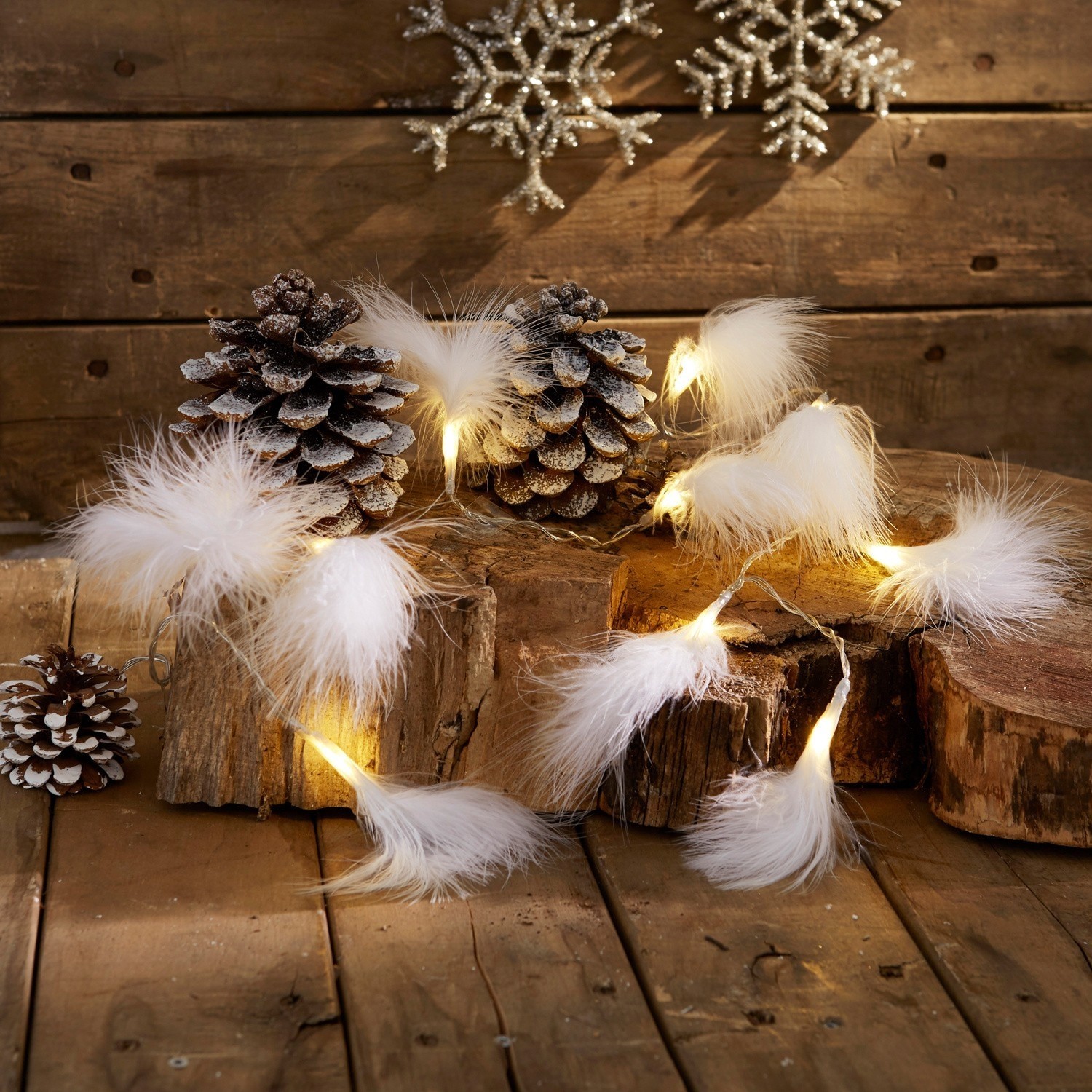 Guirlande lumineuse avec plumes blanches sur fond en bois avec pommes de pin et décorations hivernales