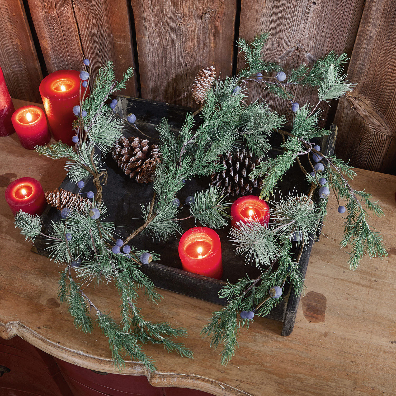 Guirlande Virpi Decoratieve krans van groene takken, dennenappels en rode kaarsen op een houten tafel