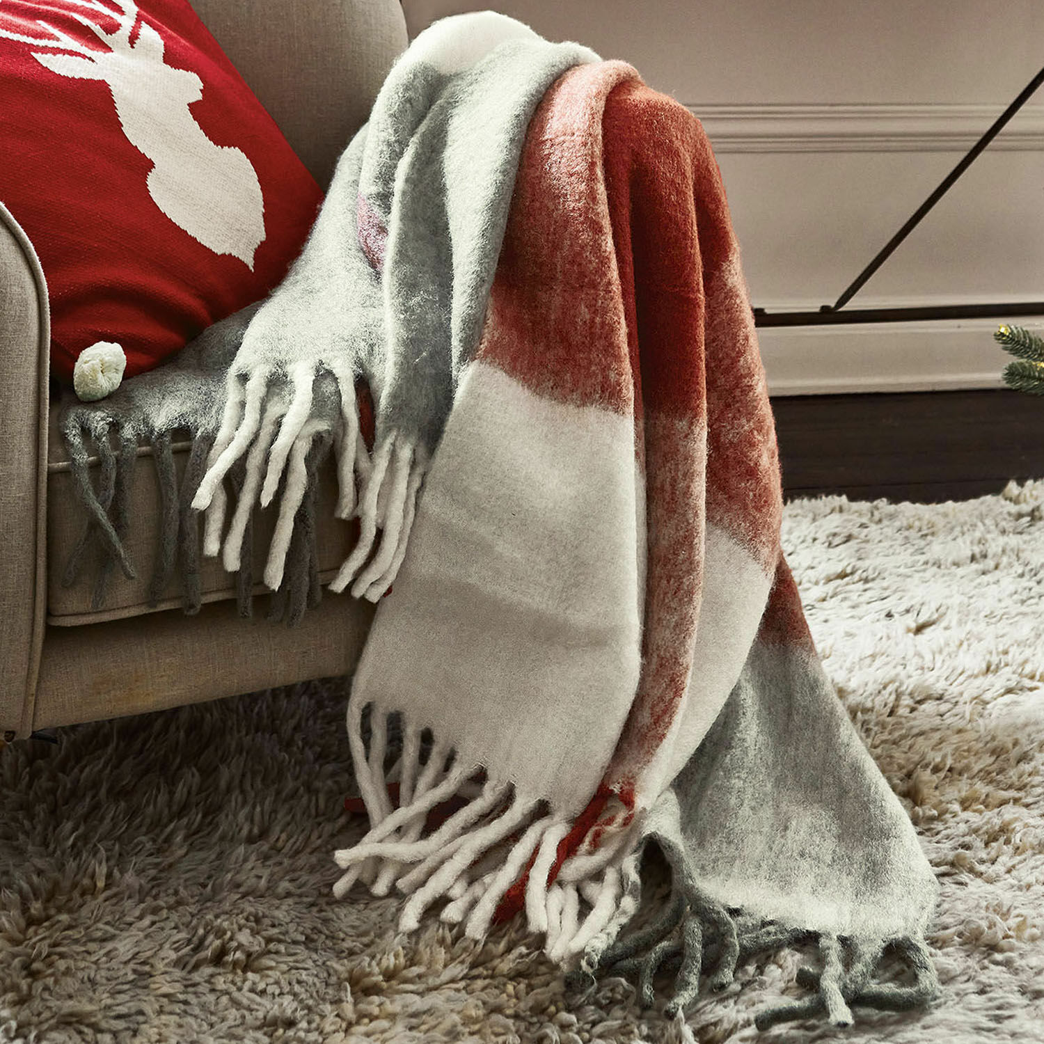 Plaid McGreg Plaid doux à franges en gris, blanc et rouge posé sur un canapé beige, décoration cosy pour salon