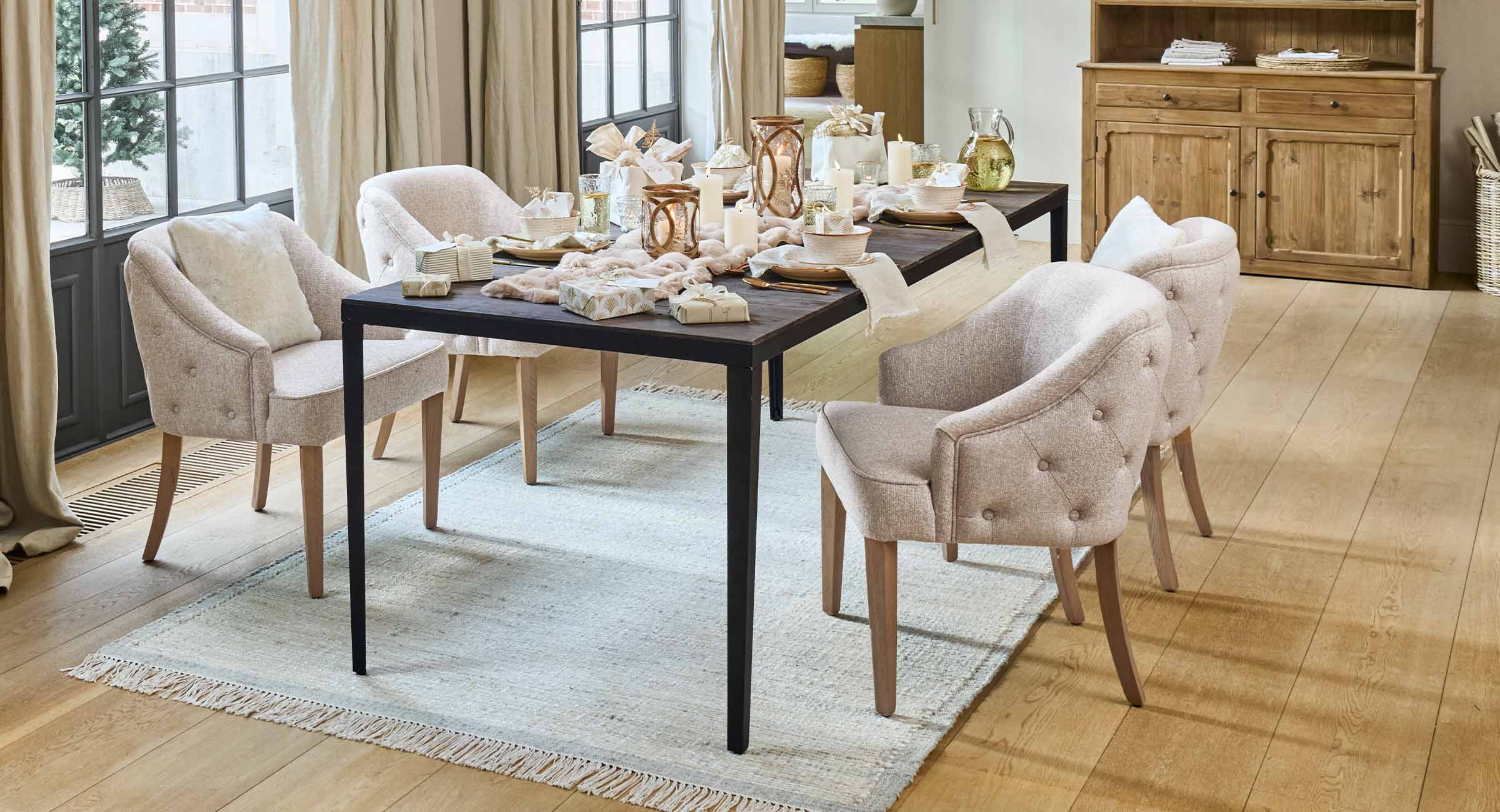 Lichtbeige gestoffeerde stoelen met houten poten bij een donkere tafel met kaarsen en decoraties in eetkamer