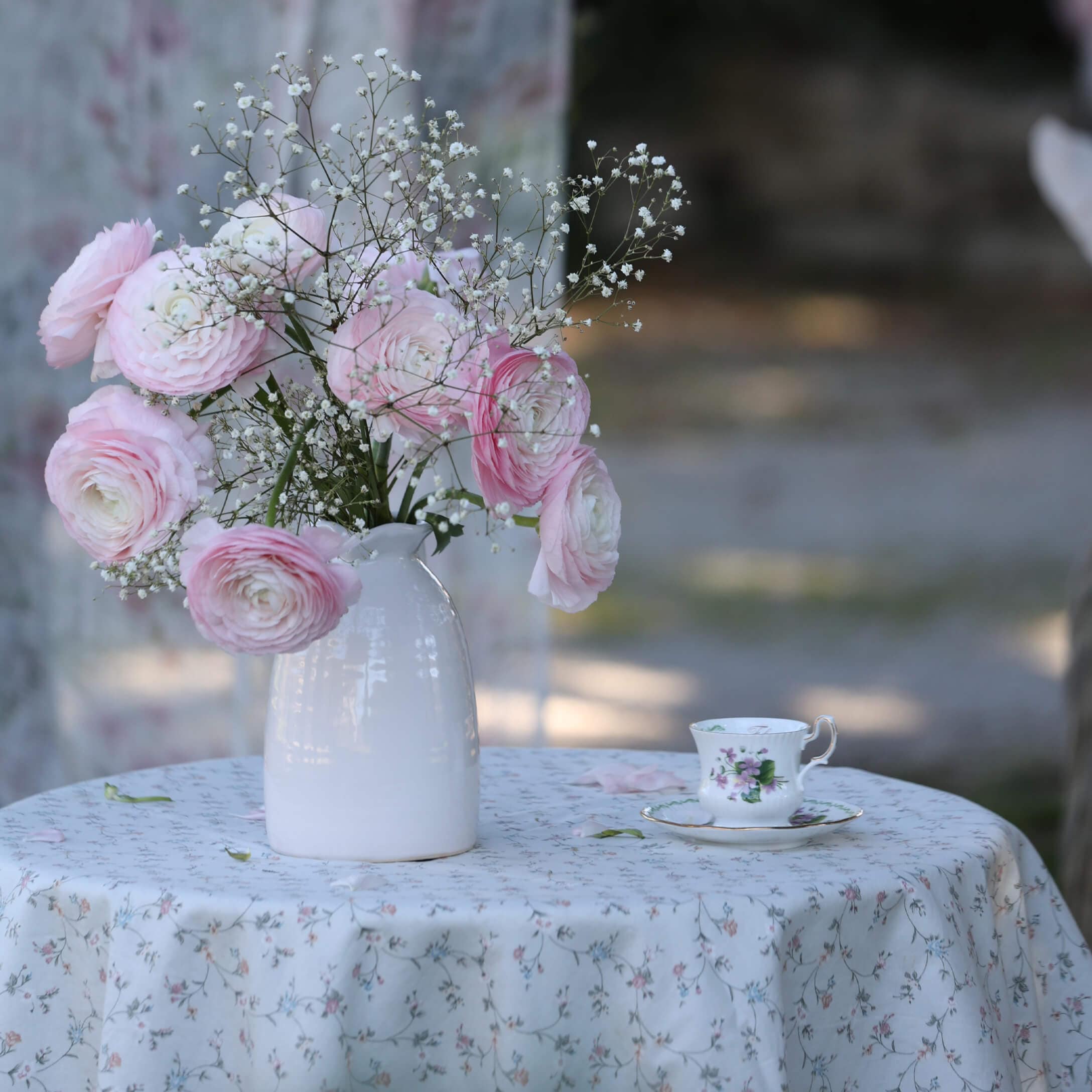 Bouquet de fleurs roses et blanches dans un vase en céramique blanche sur une table avec nappe fleurie